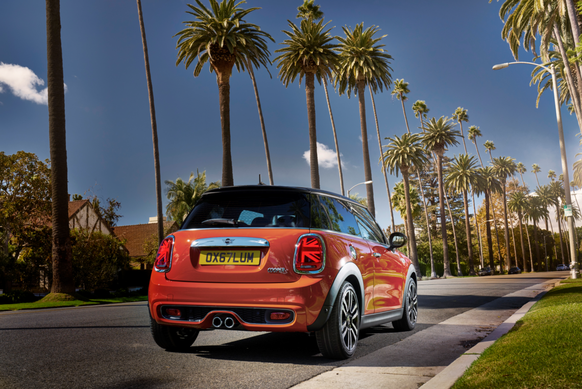 Copper colored Mini Cooper driving past palm trees
